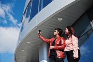 aziatisch paar dat samen staat tegen nieuw modern gebouw en selfie maakt via de telefoon. foto