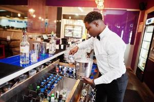 Afro-Amerikaanse barman bij bar met ijsemmer. bereiding van alcoholische dranken. foto