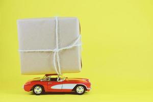 rode retro speelgoedauto die een geschenkdoos levert voor de feestdagen op een gele achtergrond met kopieerruimte foto