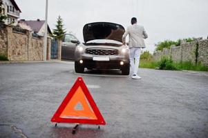 noodgevallen rode gevarendriehoek op het verkeersbord gebroken suv auto van afrikaanse man. foto