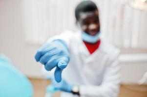 focus op vinger van Afro-Amerikaanse mannelijke arts in masker zittend op kliniek. foto