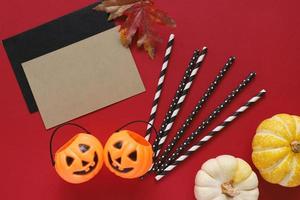 platliggende stijl van halloween-feestconcept met decoratieve pompoenen en zwart fancy stro met lege kaart op rode achtergrond foto