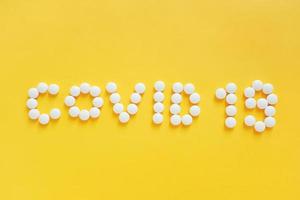 plat leggen van medicijnpillen vorm als woord covid 19 op gele achtergrond, gezondheidszorgconcept en voorkomen van de verspreiding van pandemische covid-19 en coronavirus foto
