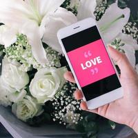 hand met smartphone met liefdeswoord op het scherm en boeket bloemen, Valentijnsdag en liefdesconcept foto