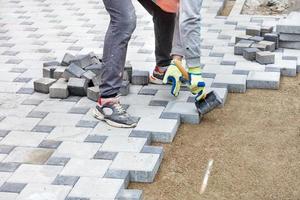 een arbeider in handschoenen legt tegels met een rubberen hamer en let daarbij op het vereiste patroon. foto