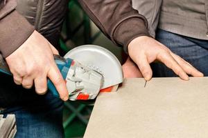 in de hand van een arbeider snijdt een slijper met een diamantschijf een keramisch-metalen plaat. foto