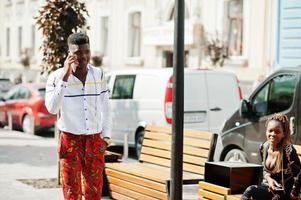 portret van knappe stijlvolle Afro-Amerikaanse model man in rode broek en wit overhemd met mobiele telefoon bij de hand. foto