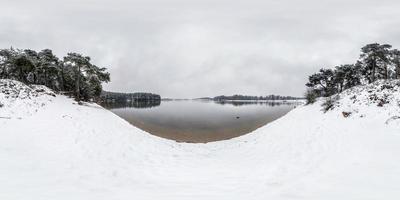 winter volledig bolvormig hdri-panorama 360 graden hoekweergave in de buurt van meer in besneeuwd dennenbos met grijze bleke lucht in equirectangular projectie. vr ar inhoud foto