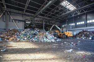 graafmachine stapelt afval in grote stapel bij het sorteren van moderne afvalverwerkingsfabriek. gescheiden en sorteren van afvalinzameling. recycling en opslag van afval foto