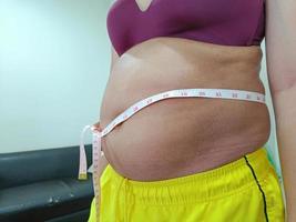 vooraanzicht. sjofele dikke aziatische vrouw die haar buik toont. u moet voor uw gezondheid en lichaamsbeweging zorgen. foto