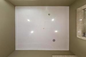 kijk omhoog op verlaagd plafond met halogeenspots lampen en gipsplaatconstructie met brandalarmsensor in lege kamer in appartement of huis. spanplafond wit en complexe vorm. foto