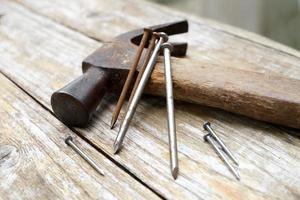 hamer en spijkers op houten ondergrond, hout en roest hoofd ijzeren hamer liggend op een houten bord met outdoor workshop. foto