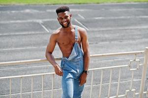 knappe sexy Afro-Amerikaanse naakte torso man op jeans overall gesteld in het stadion. modieuze zwarte man portret. foto