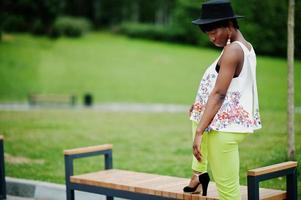 geweldige Afro-Amerikaanse model vrouw in groene broek en zwarte hoed gesteld in het park. foto