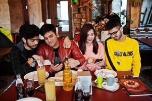 groep aziatische vrienden die in café zitten. gelukkige indiase mensen die samen plezier hebben, op de bank zitten en naar mobiele telefoons kijken. foto