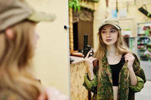 militair meisje in camouflage-uniform met revolverpistool bij de hand tegen legerachtergrond op schietbaan. foto