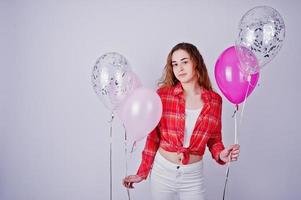 jong meisje in rood geruit overhemd en witte broek met ballonnen tegen een witte achtergrond op studio. foto