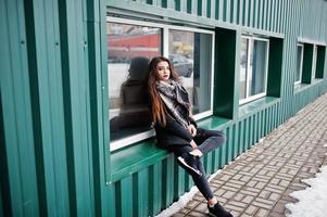 brunette stijlvolle casual meisje in sjaal tegen groene metalen muur. foto