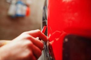 autoservicemedewerker plaatste anti-grindfilm op een rode carrosserie in de detailleringsvoertuigwerkplaats. autobescherming met speciale folies. foto