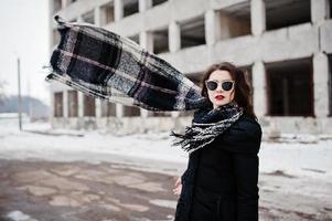 brunette stijlvolle casual meisje in sjaal en zonnebril tegen verlaten fabrieksplaats. sjaal in de lucht. foto