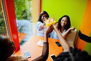 vier jonge afrikaanse meisjes juichen met sinaasappelsap terwijl ze in een felgekleurd fastfoodrestaurant zitten. foto