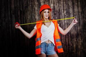 ingenieursvrouw in oranje beschermt helm en bouwjas tegen houten meetlint als achtergrond. foto