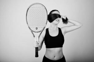 zwart-wit portret van een mooie jonge vrouw in sportkleding die een tennisracket vasthoudt terwijl hij tegen een witte achtergrond staat. foto