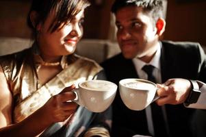 elegante en modieuze Indiase vrienden paar vrouw in saree en man in pak zittend op café en cappuccino drinken. foto