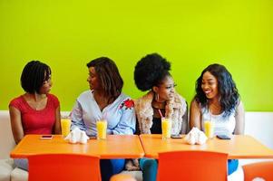 vier jonge afrikaanse meisjes met sappen zitten in felgekleurd fastfoodrestaurant. foto