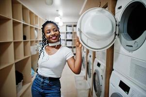 vrolijke afro-amerikaanse vrouw in de buurt van wasmachine in de zelfbedieningswasserette. foto