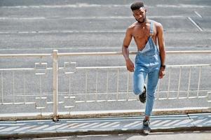 knappe sexy Afro-Amerikaanse naakte torso man op jeans overall gesteld in het stadion. modieuze zwarte man portret. foto