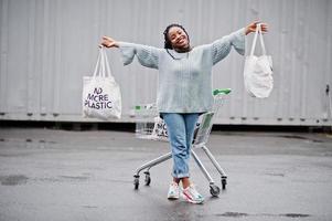 geen kunststof meer. Afrikaanse vrouw met winkelwagentje en eco-tassen poseerde buitenmarkt. foto