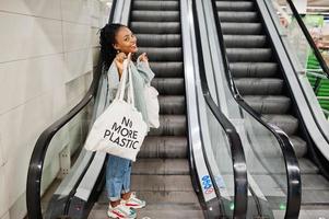 Afrikaanse vrouw met boodschappentassen op roltrap in winkelcentrum. foto