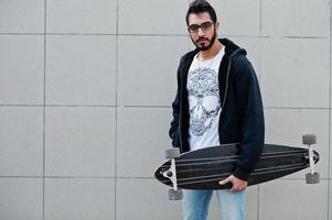 straatstijl Arabische man in brillen met longboard gesteld tegen grijze muur. foto