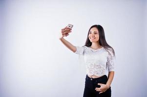 portret van een jonge mooie vrouw in witte top en zwarte broek die selfie neemt. foto