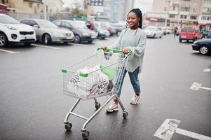 Afrikaanse vrouw met winkelwagentje stelde buitenmarkt in de buurt van parkeerplaats. foto