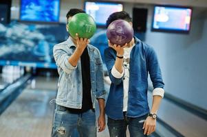 twee vrienden in jeansshirt bij bowlingclub die ballen op handen houden en hun gezicht verbergen. foto