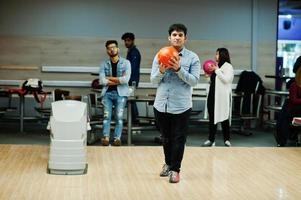 Zuid-Aziatische man in jeans shirt staande op bowlingbaan met bal op handen. man bereidt zich voor op een worp. foto