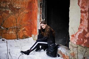 modieuze lange benen brunette model in lange zwarte mantel gesteld buiten op winterdag tegen oude grunge muur. foto
