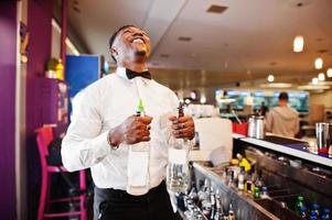 Afro-Amerikaanse barman bij bar met twee flessen. bereiding van alcoholische dranken. foto