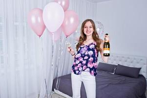 gelukkig meisje met gekleurde ballonnen op bed op kamer met glazen en fles champagne. verjaardag thema vieren. foto