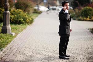 elegante Zuid-Aziatische Indiase zakenman in zwart pak spreken op mobiele telefoon. foto