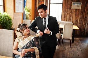 elegante en modieuze Indiase vrienden paar vrouw in saree en man in pak poseerde indoor cafe. foto