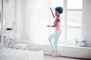 jonge Afro-Amerikaanse vrouw in roze hemd tegen raam. perfecte ochtend. foto