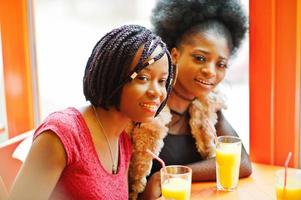 twee jonge Afrikaanse meisjes met sappen zitten in felgekleurd fastfoodrestaurant.a foto