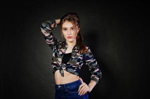 knappe brunette meisje draagt militair shirt en spijkerbroek, poseren in studio tegen een grijze achtergrond. studiomodel portret. foto