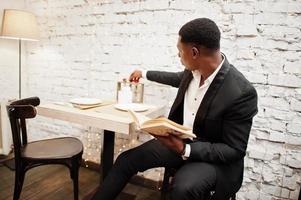 sterke krachtige Afro-Amerikaanse man in zwart pak zit in café en lees boek. foto