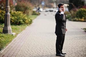 elegante Zuid-Aziatische Indiase zakenman in zwart pak spreken op mobiele telefoon. foto