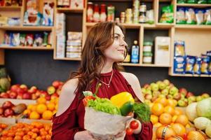 meisje in het rood met verschillende groenten in de fruitwinkel. foto