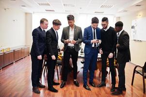 zes multiraciale zakenmannen die op kantoor staan en mobiele telefoons gebruiken. diverse groep mannelijke werknemers in formele kleding met mobiele telefoons. foto